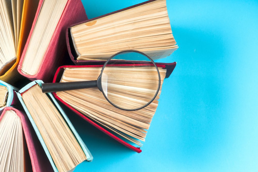 A group of nondescript books placed on a table with a magnifying glass